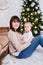 Christmas, happiness and family concept - happy mother sitting with little baby girl near decorated christmas tree