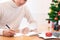 Christmas and Happy New Year blessing concept. Man wearing white sweater writing and sending greeting card