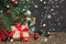 Christmas holiday background. Gifts with a red ribbon, Santa`s hat and decor under a Christmas tree on a wooden board.