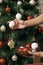 Christmas holiday green and red decoration. Guy`s hands ornamenting the pine tree with a white ball decoration