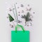 Christmas holiday shopping concept. Green bag with festive purchases, decor, glitter confetti on grey background