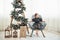 Christmas and holidays conception. Cute little girl is sits on the chair near ladder decorated with stars and gift boxes on the