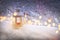 Christmas lantern with burning candle shines on snow and tree branches with yellow bokeh. Winter season and snowfall