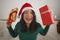 Christmas lifestyle portrait of young beautiful and happy Asian Chinese woman on bed in Santa Claus hat holding xmas presents and