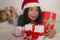 Christmas lifestyle portrait of young beautiful and happy Asian Korean woman on bed in Santa Claus hat holding lot of xmas