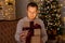 Christmas and magic concept - portrait of happy surprised young man opening gift box in decorated dark room with Christmas tree