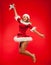 Christmas, x-mas, winter, concept - smiling woman in santa helper hat with gift box, happiness jump for joy over red