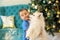 Christmas morning: happy little boy embracing white samoyed puppy under decorated fur tree. Dog is licking cheek of child