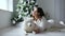 Christmas morning, woman poses with white dog in cozy atmosphere on photoshoot near decorated new year tree