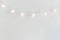 Christmas New Year Background. Hanging Pastel Golden Cotton Balls Garland White Wall Background. Scandinavian Style. Lights