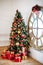 Christmas and New Year decorated white interior room with presents and New year tree with red decor ball. Grey sofa and