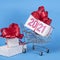 Christmas and New Year delivery concept. 2021 text on gift box with red ribborn and shopping trolley. Blue background.