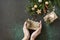 Christmas or New Year layout. Female hands hold Christmas present on a dark green stone background. Holiday concept. Flat lay,