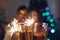 Christmas and New year party concept. Couple in love burning sparklers by illuminated Christmas tree with champagne
