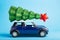 Christmas New Year tree with red star on top of blue car toy roof. Blue color background. Creative miniature Xmas tree on car