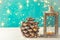 Christmas New Years greeting card with pine cone lantern with burning candle golden garland lights on turquoise background