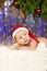 Christmas newborn baby in santa hat. Winter child on winter wonderland background of blurred lights