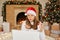 Christmas online congratulation, girl in santa claus hat and white sweater talks with somebody using laptop for video call,