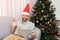 Christmas online congratulations. Smiling man near chrstmas tree using tablet for video call friends and parents