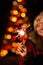 Christmas photography. the girl holds a sparkler in her hand, the lights of garlands on the tree are visible from behind.
