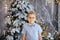 Christmas portrait of happy child boy with big glasses indoor studio, snowy winter decorated tree on background. New Year Holidays