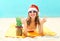 Christmas portrait pretty young smiling woman in red santa hat and pineapple lying on beach over sea