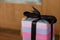 A christmas present with black bow and purple pink wrapping papper, neatly wrapped. Soft glow of christmas lights in the blurred