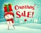 Christmas Sale! Cheerful snowman holds up gift present in Christmas snow scene winter landscape.