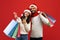 Christmas sales and shopping. Arab couple with shopper bags and credit card, posing in Santa hats on red background