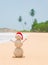 Christmas sandy snowman in santa hat at palm ocean beach