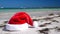 Christmas Santa Claus hat on tropical sandy beach with calm waves