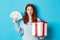 Christmas and shopping concept. Excited redhead girl looking at camera, holding big New Year gift and dollars, buying