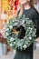 Christmas shopping. Green Christmas wreath in female hands. Decorated with gray elements, cotton and silver ball