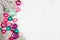 Christmas side border with pink, purple and teal ornaments and snowy branches, above view on a white wood background