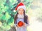 Christmas smiling child little girl, santa red hat with ball near tree