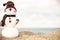 Christmas snowman in red santa hat and sunglasses at sunny beach. Holiday concept for New Years Cards.