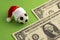 Christmas sports betting. Red Santa Claus hat is dressed on a souvenir soccer ball. Two bills of one dollar on a green background