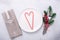 Christmas table place setting with empty white plate, candy canes, cutlery with festive decorations on stone background