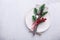 Christmas table place setting with empty white plate, candy canes, fir branch and cutlery with festive decorations on stone
