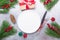 Christmas table place setting with empty white plate, gift box, cutlery with festive decorations on stone background