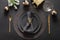Christmas table setting with dark black plates, gold deer ring and gold cutlery. Golden gilded decorations.