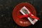 Christmas table setting , red plate, vintage cutlery and napkin tied with a ribbon on a dark rustic background.Top view, flat lay