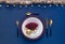 Christmas table setting in white, gold, burgundy on dark blue linen tablecloth