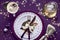 Christmas table setup with white plate, golden utensils and gilded decorations on dark purple linen table cloth. Flat lay, top