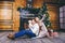 Christmas theme. young family with blond boy of one year sits on wooden floor against background of a Christmas tree with gifts an