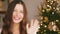 Christmas time and holiday greetings concept. Happy woman smiling and waving hand, decorated xmas tree lights on