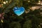 Christmas toy in the shape of a heart with the image of waves of the blue sea hangs on a green tree