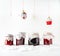 Christmas toys hanging on rope, red fruit jam in glass jars standing on snowy background