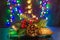 Christmas tree branch with cones and red rowan berry are on the shiny table/background. There are different colors lights.