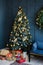 A Christmas tree with gold and blue balloons with gifts under it stands in the living room